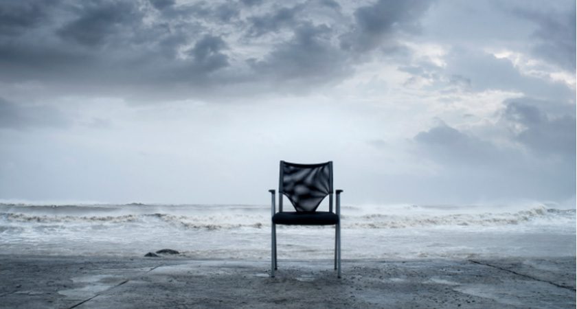 An empty chair sits on a concrete block in front of a white sea on a stormy day.