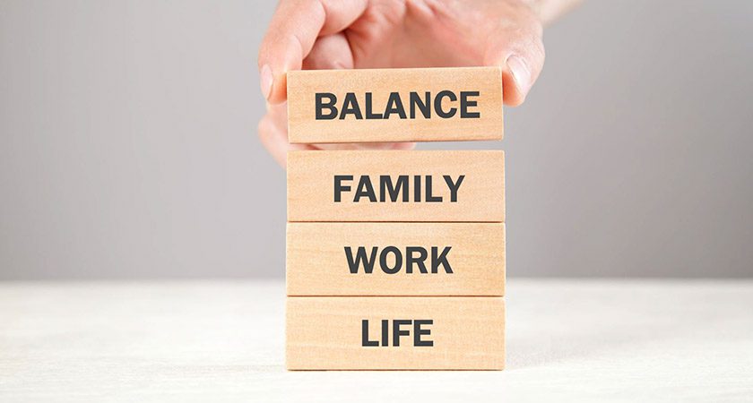 Wooden blocks are being stacked, reading from top-to-bottom "Balance, Family, Work, Life."