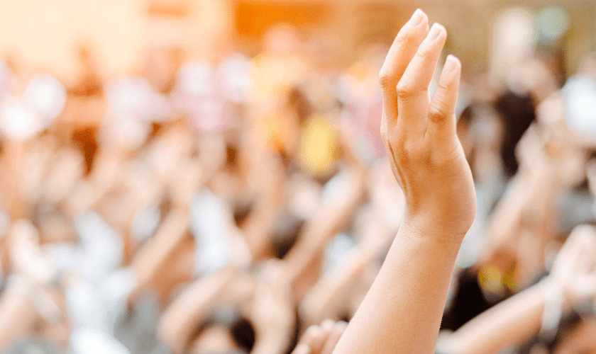 A hand is raised amongst a crowd of out-of-focus raised hands