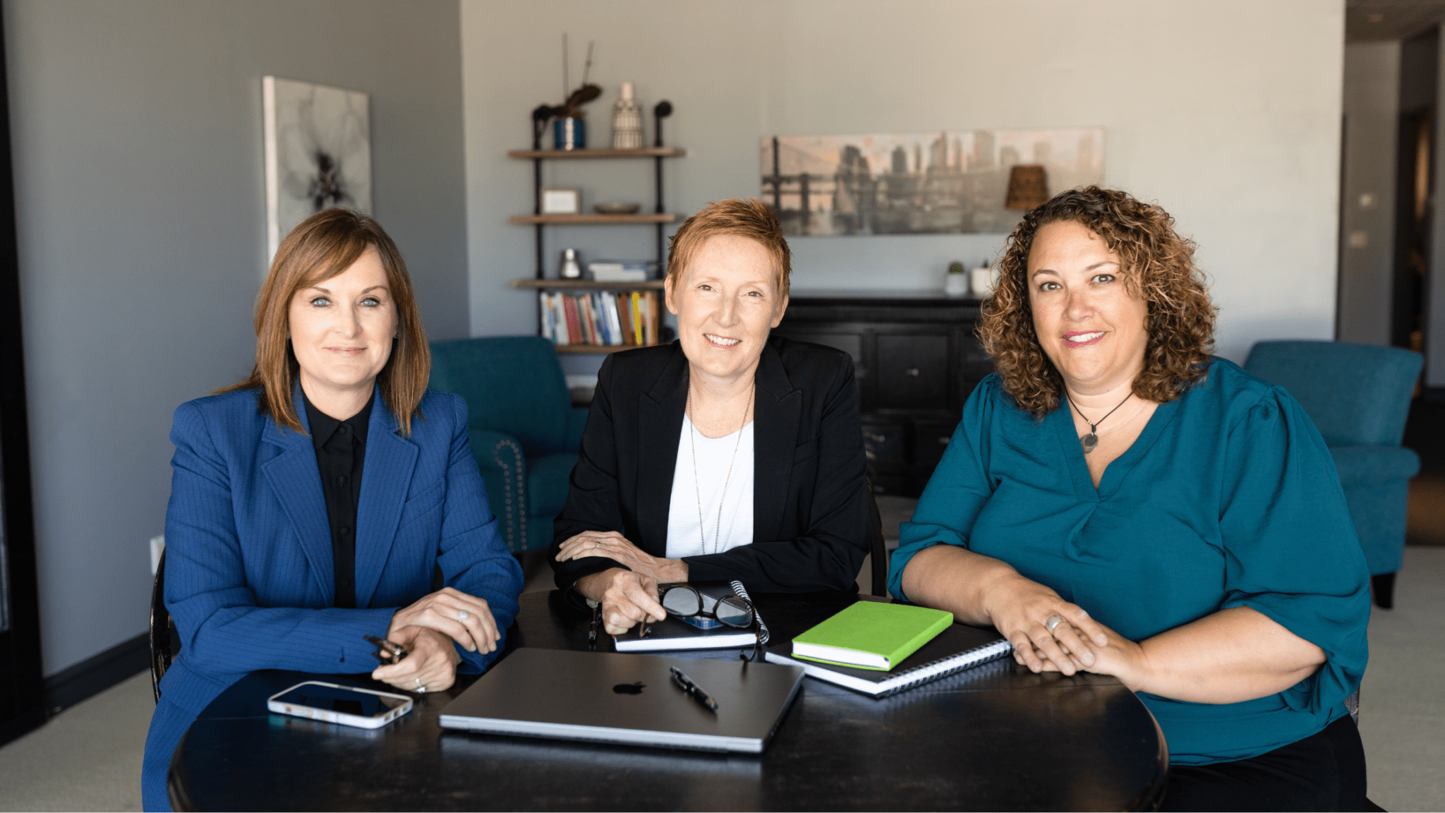 Meet the Slingshot25 Leadership Team Three women seated at table, professionally dressed and smiling